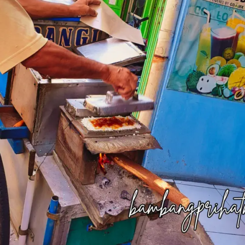 Kue Rangi: Ngidam Istri dan Petualangan Mencari Jajanan Betawi 9 Pedagang kue rangi sedang memasak kue rangi di atas cetakan kue yang dipanggang di atas api.